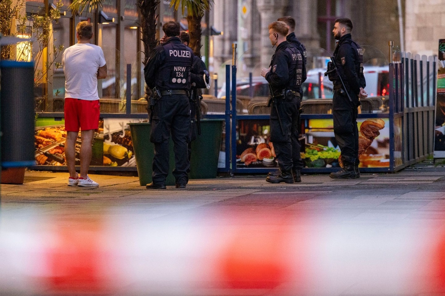 Polizisten stehen in Duisburg bei einem Einsatz neben einem Mann in Sportkleidung, der vor Ort als Zeuge befragt worden sein soll.