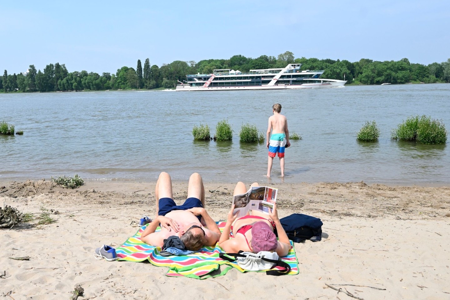 Eine Frau und ein Mann genießen am Rheinstrand die milden Temperaturen und die Sonne.